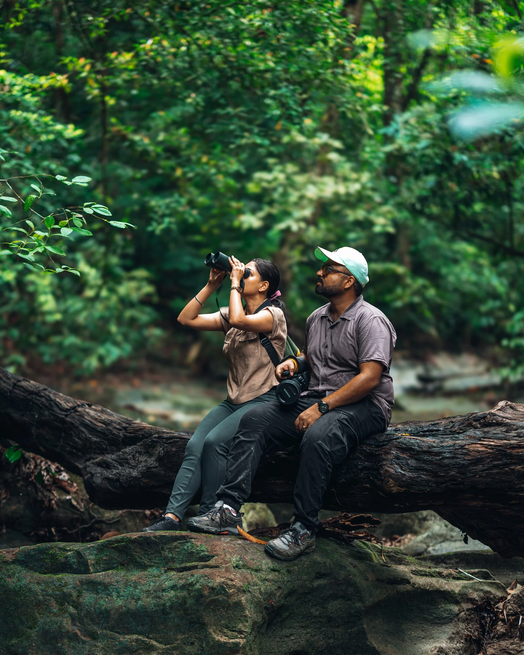 Two people in a forest, one looking through binoculars
